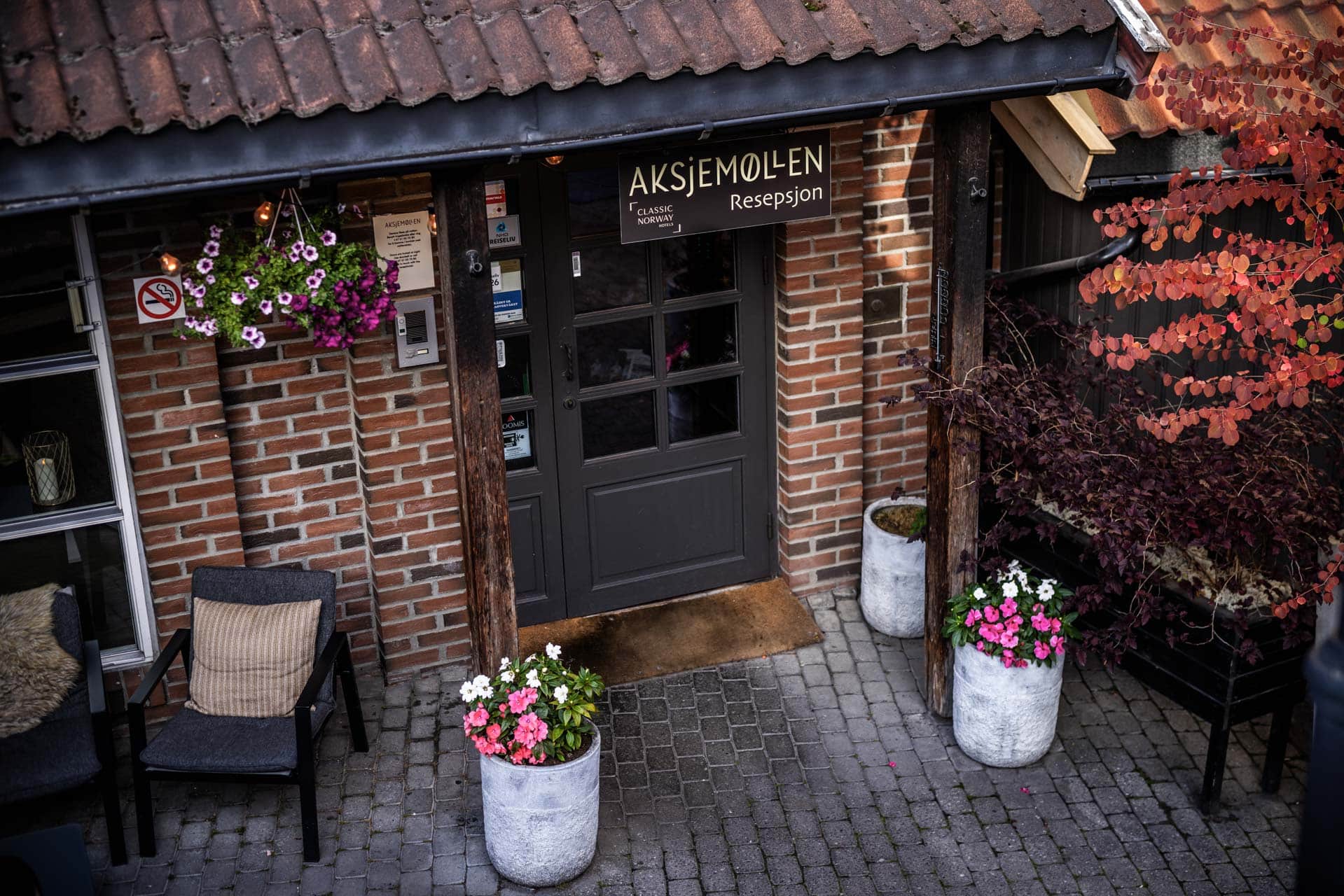 Sjarmerende inngangsparti med rustikke tredetaljer og blomster ved Aksjemøllen Boutiquehotell.
